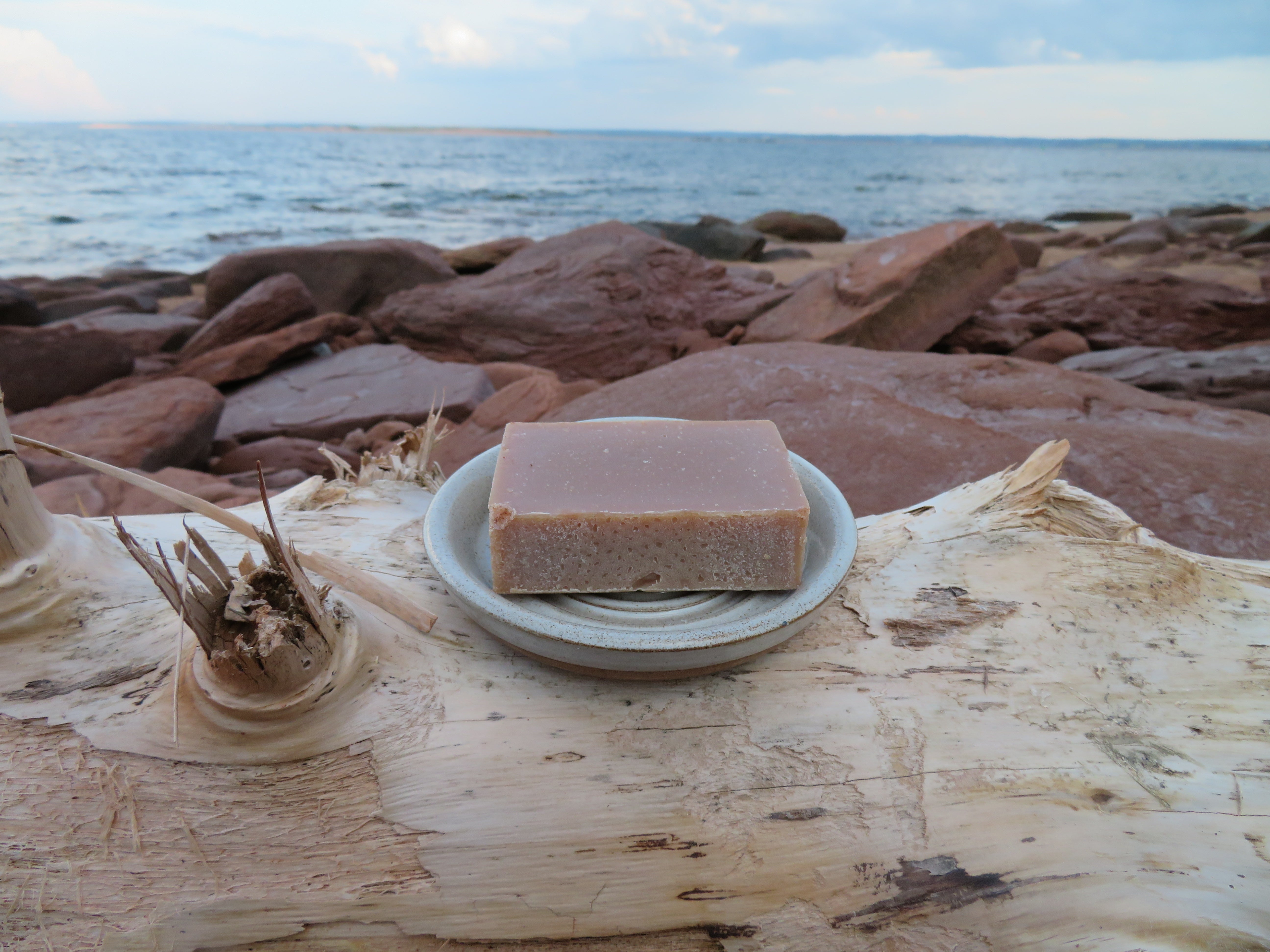 Bar of soap on a white plate with a beach and ocean in the background
