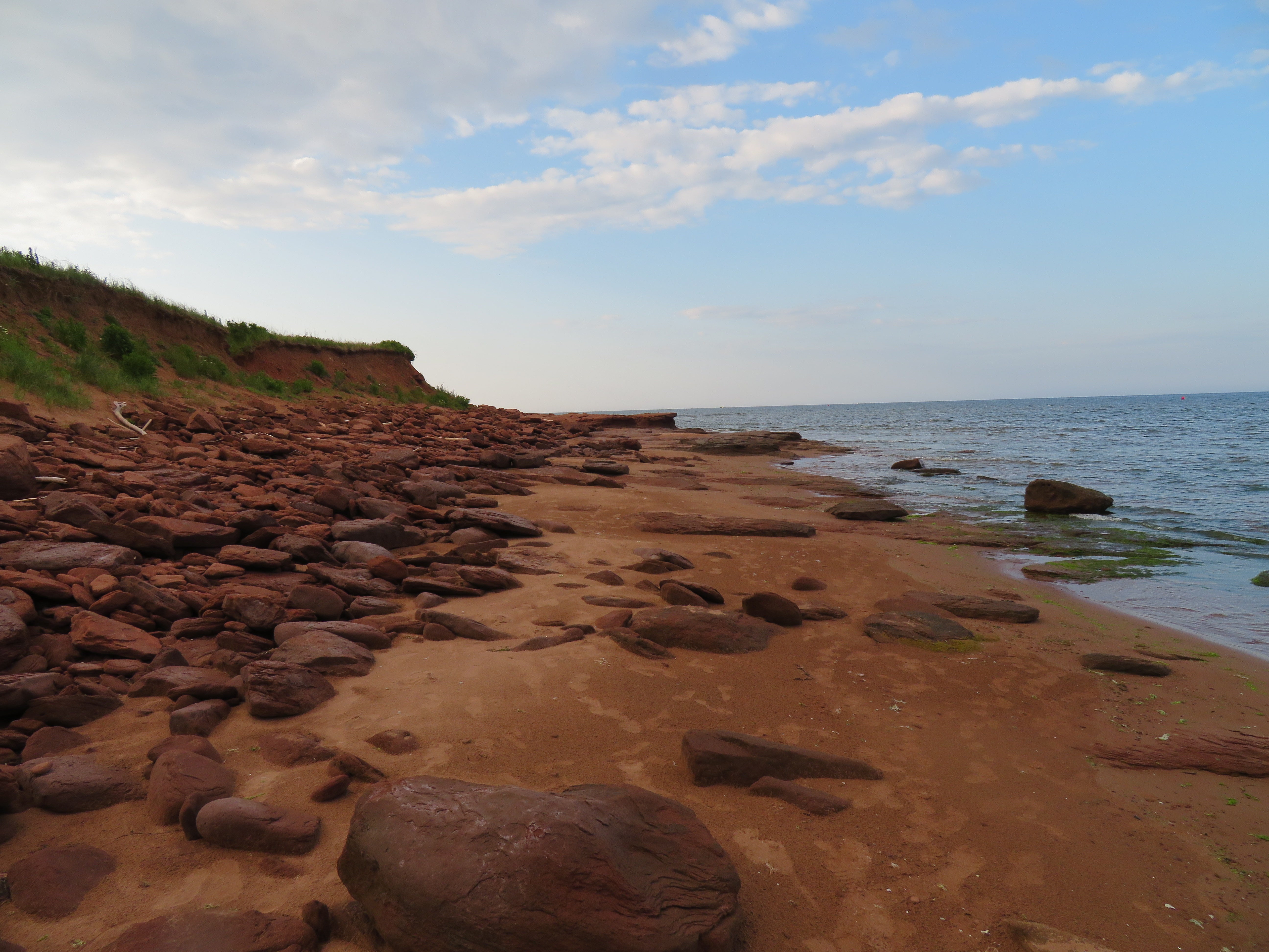 Rocks on a sandy beach with a body of water and sky in the background