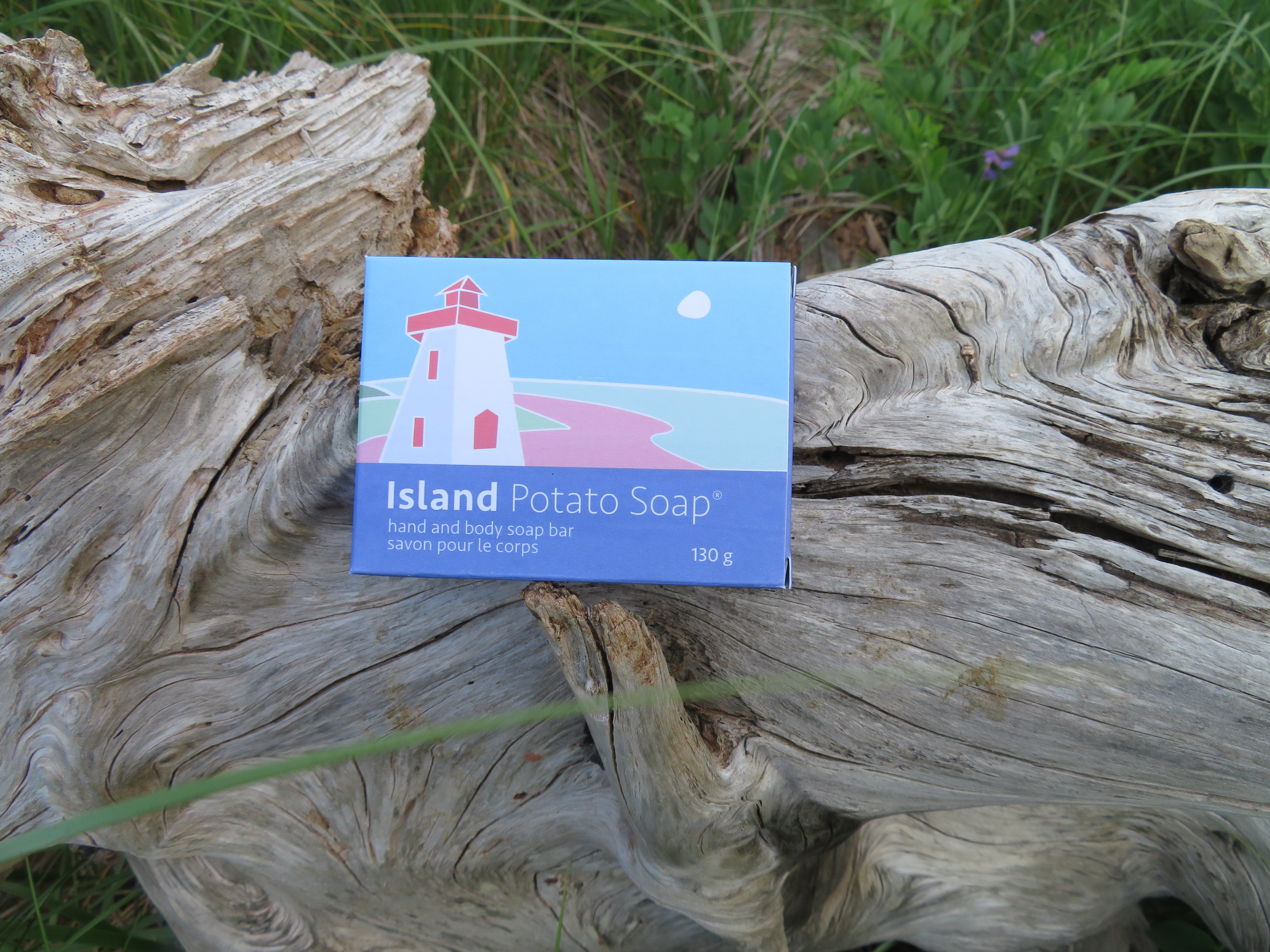 Box of Island Potato Soap on a piece of driftwood with grass in the background