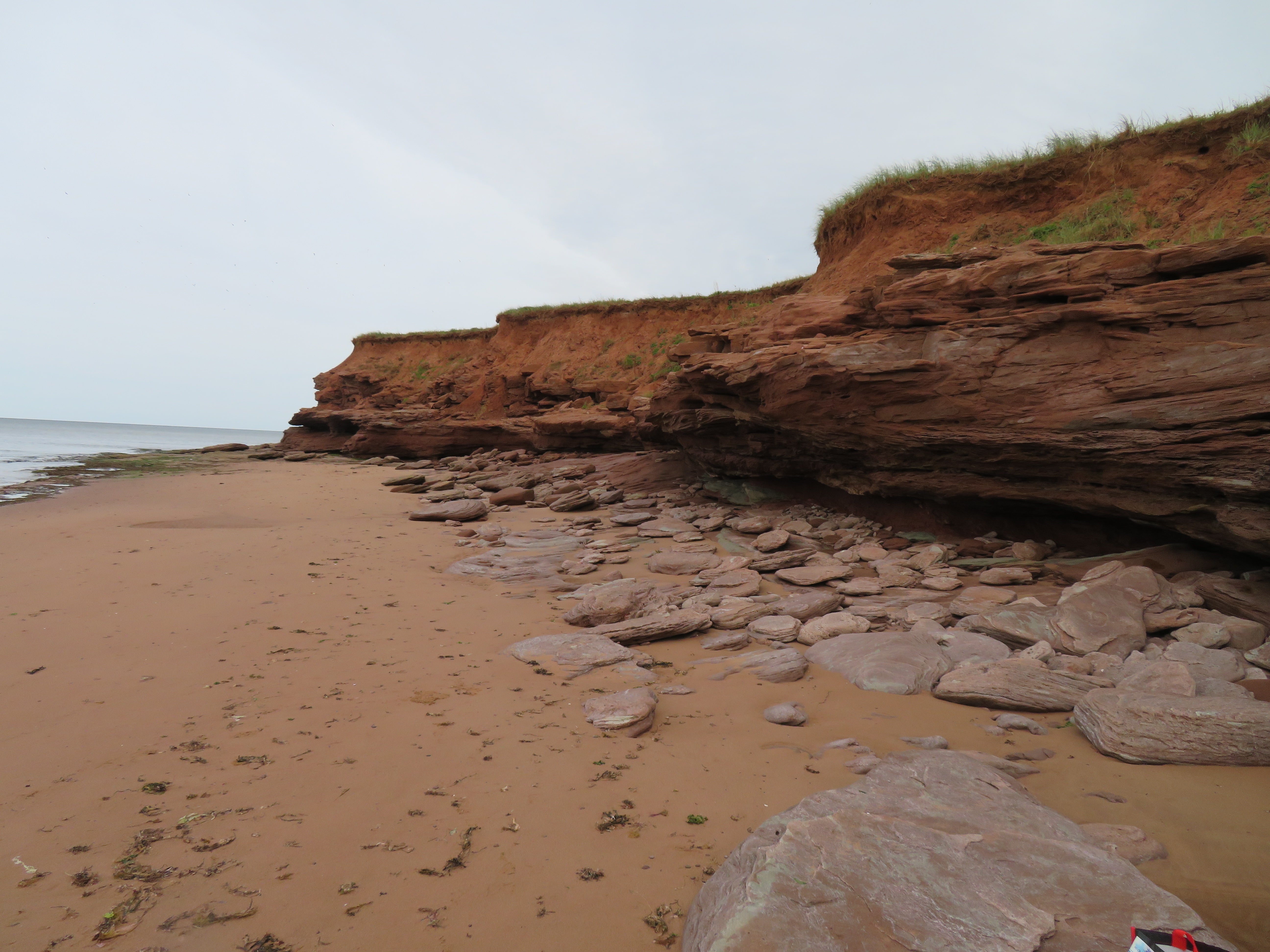 Beach with sand, rocks, and cliffs under a cloudy sky