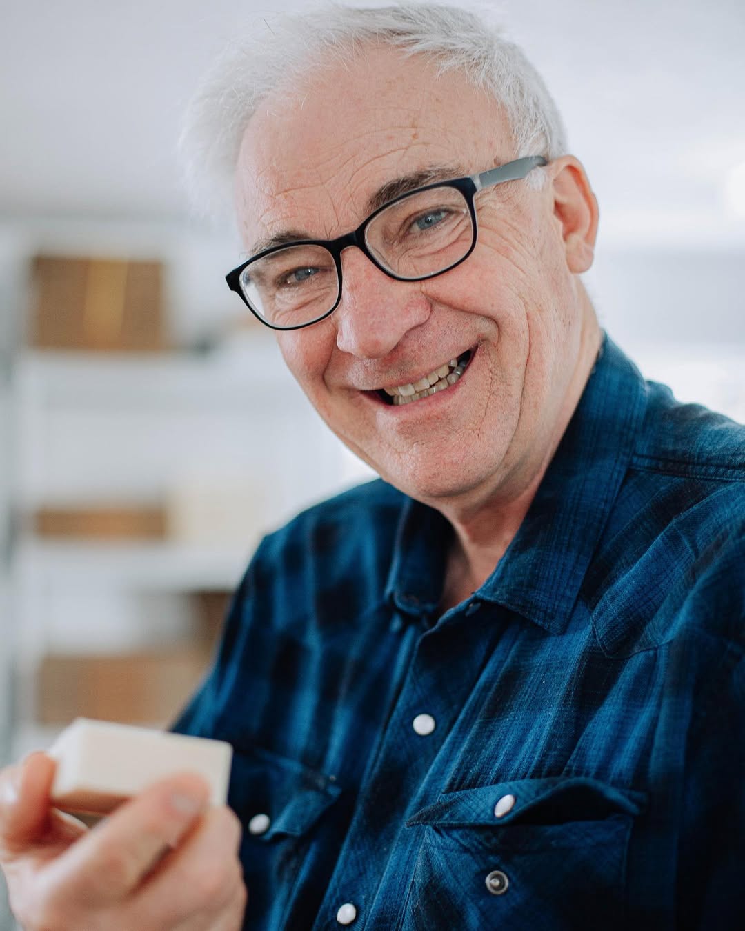 Man wearing glasses and a blue shirt holding a white object indoors