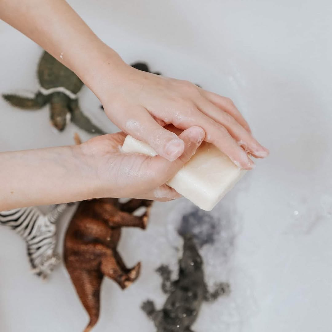 Person holding a bar of soap above a bathtub with animal prints.