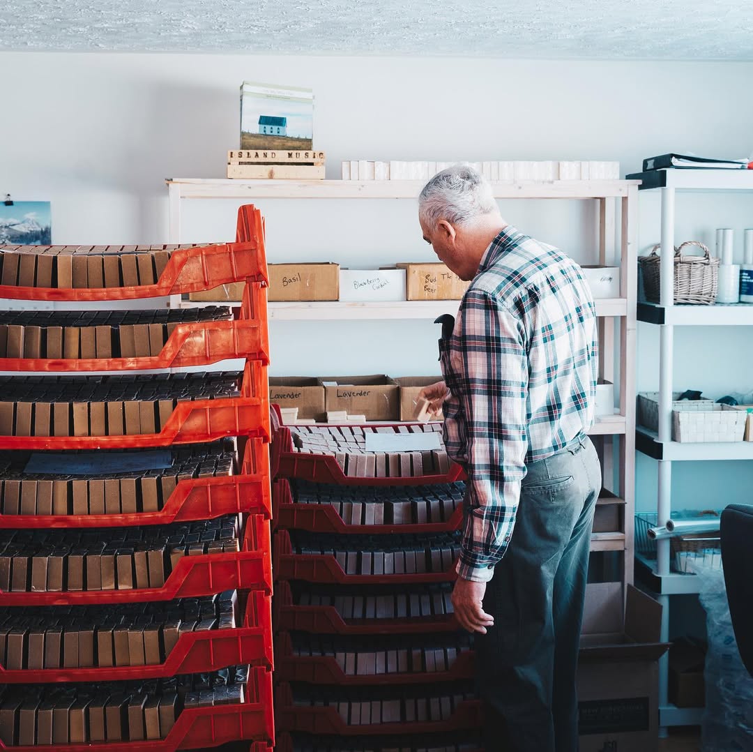 Man organizing boxes in a storage room with shelves and red crates.