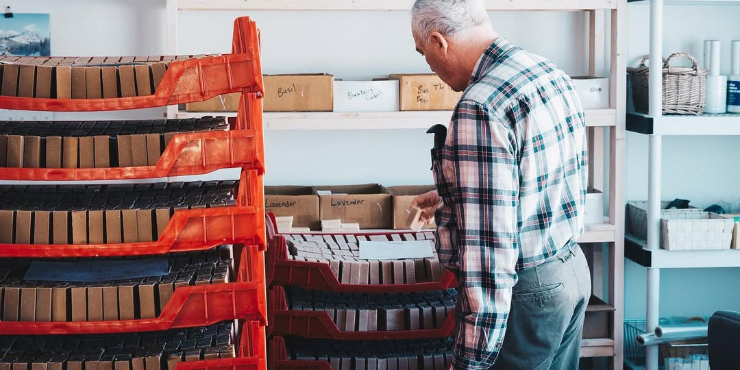 Man organizing boxes in a storage room with shelves and red crates.