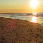 Sunset at a beach with waves and a person in the distance.
