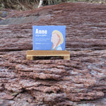 Small blue card with a woman's face on it, placed on a wooden stand against a natural background.