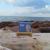 Bar of soap on a wooden stand with 'Anne' branding against a beach background