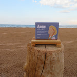 Box labeled 'Anne' on a wooden stump with a beach and ocean background