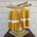 Row of yellow candles on a wooden stand against a tiled wall.