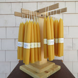 Row of yellow candles on a wooden stand against a tiled wall.