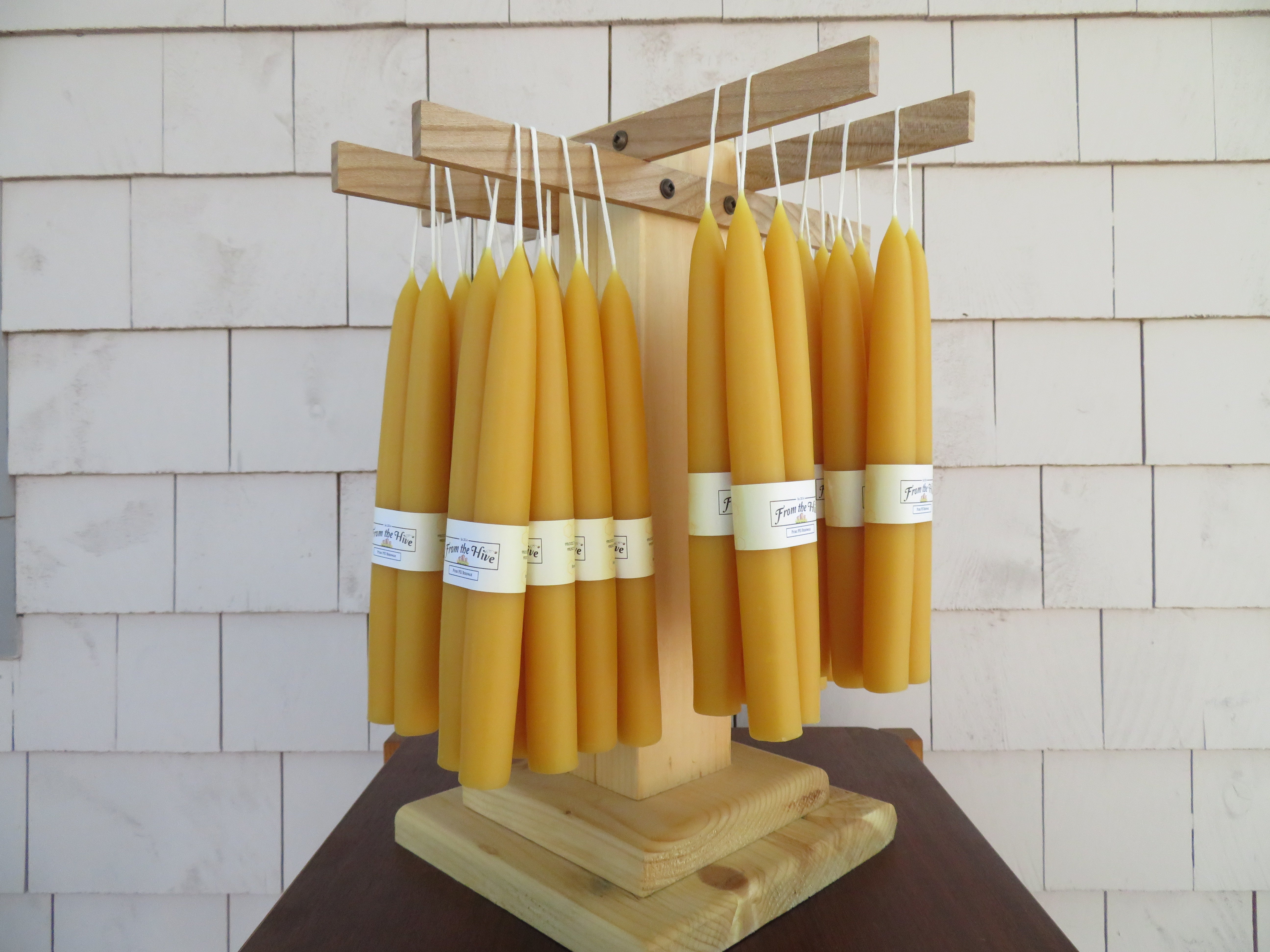 Row of yellow candles on a wooden stand against a tiled wall.