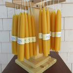 Yellow candles with labels on a wooden holder against a tiled wall.