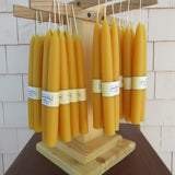 Yellow candles with labels on a wooden holder against a tiled wall.