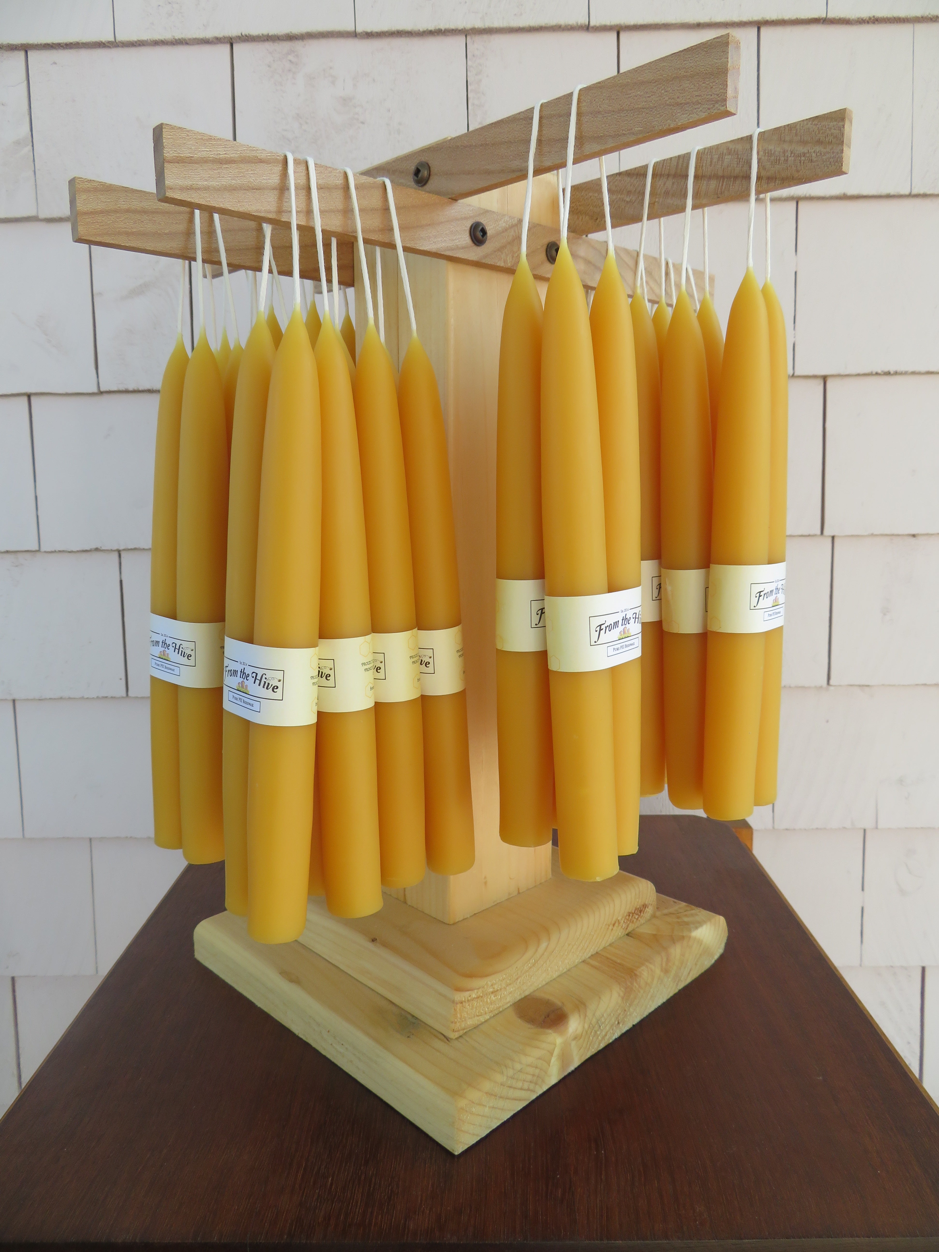Yellow candles with labels on a wooden holder against a tiled wall.