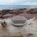 Bar of soap on a white plate with a beach and ocean in the background