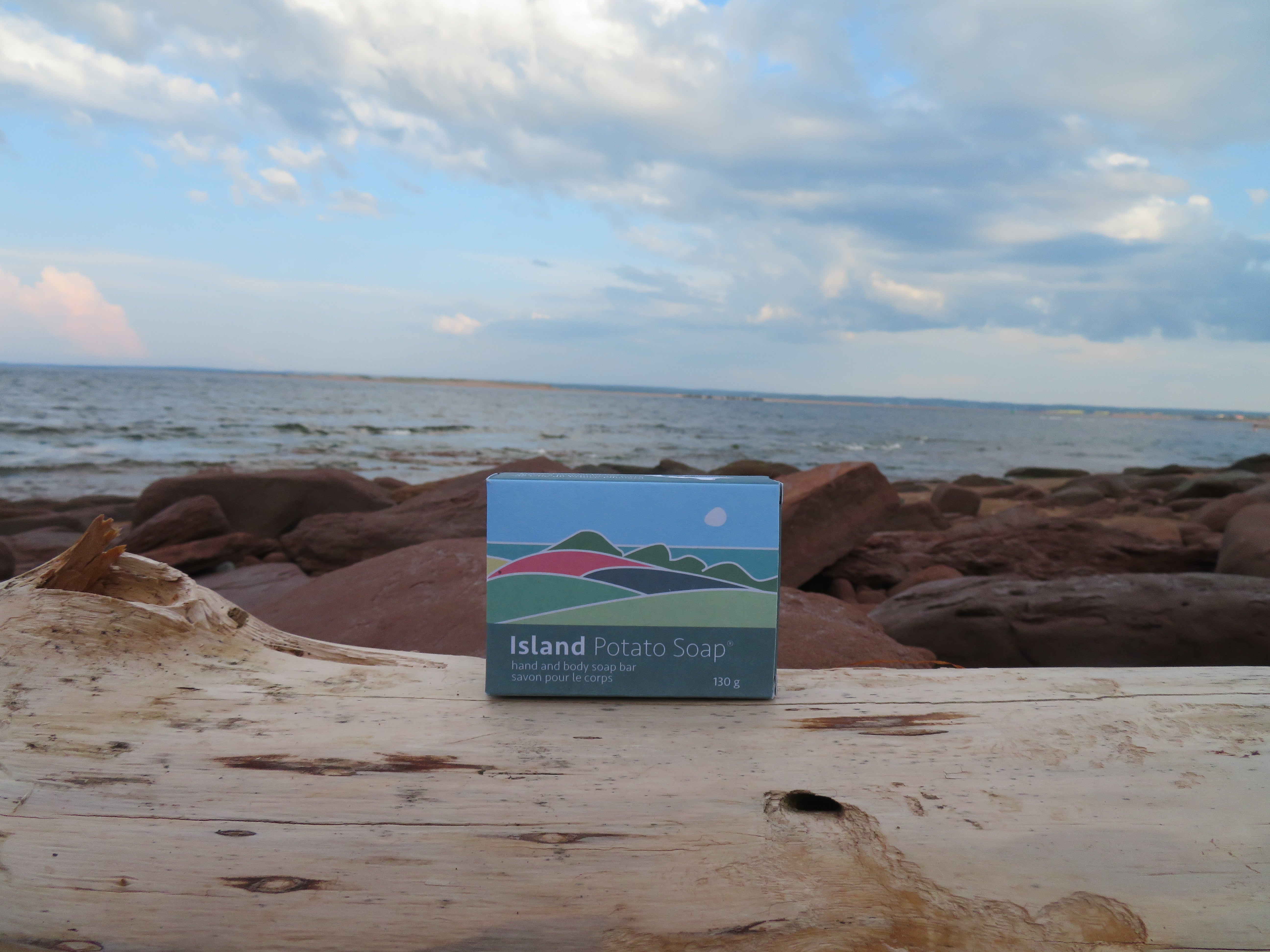 Island Potato Soap packaging on a piece of driftwood with a beach background
