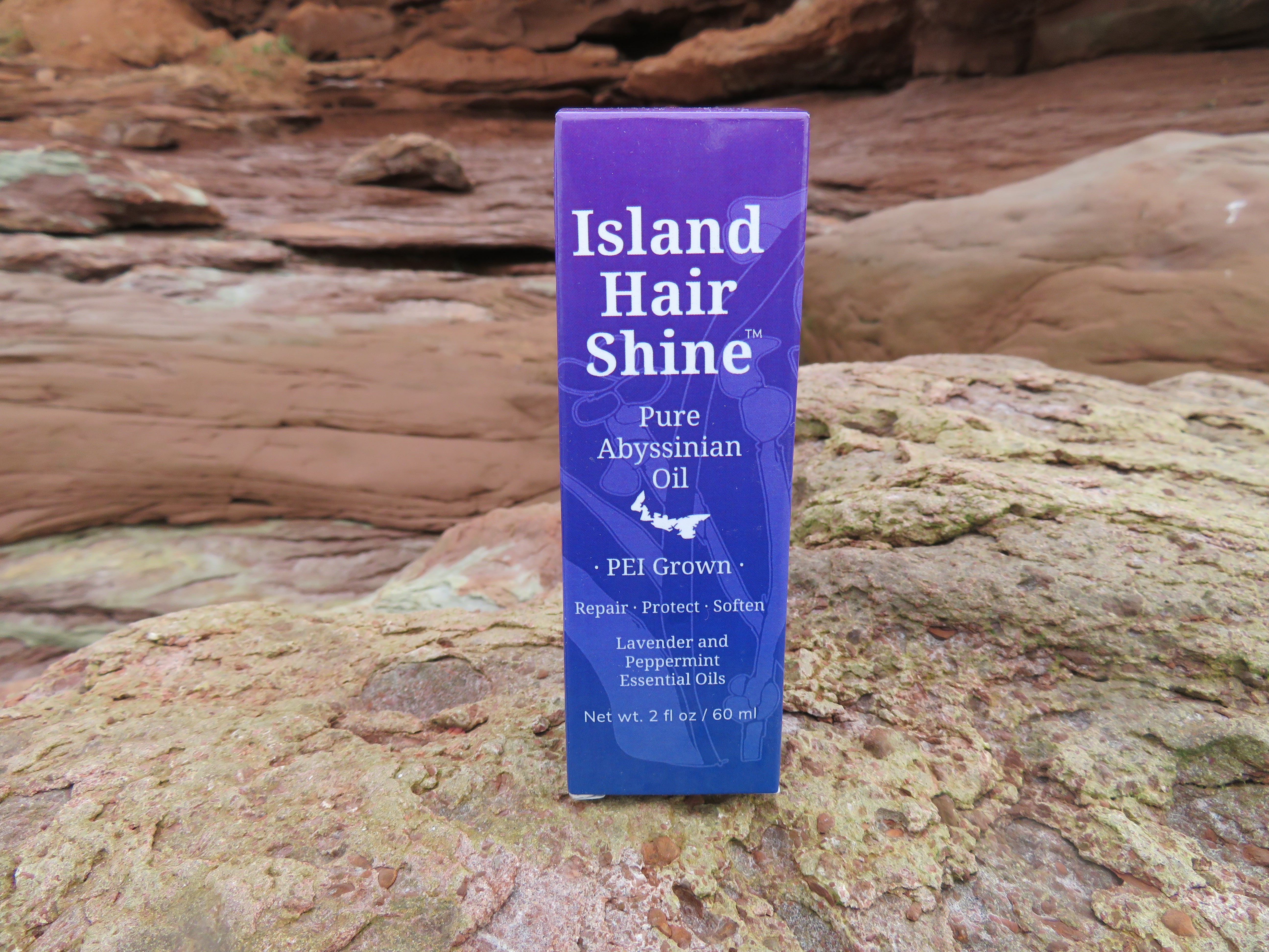 Island Hair Shine product packaging on a rocky surface