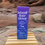 Island Hair Shine product on a wooden block with a natural rock background