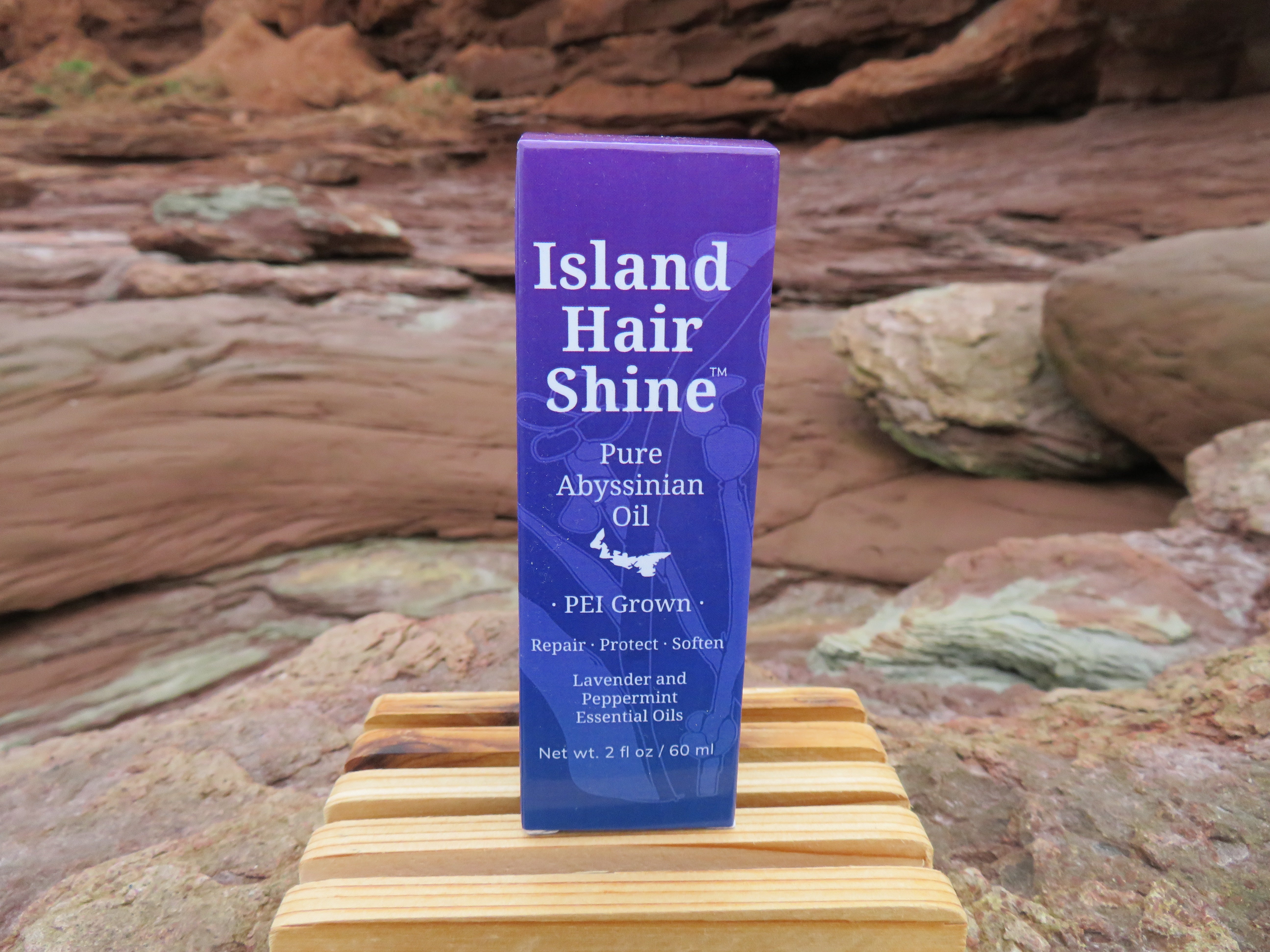Island Hair Shine product on a wooden block with a natural rock background