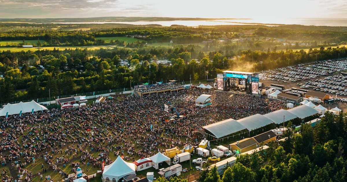 Large outdoor concert with stage and crowd in a scenic landscape