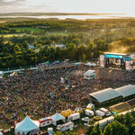 Large outdoor concert with stage and crowd in a scenic landscape