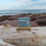 Book titled 'Marilla' on a wooden stand with a scenic ocean background