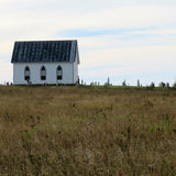 Small white church with a black roof in a grassy field under a clear sky.