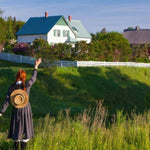 Person with a hat standing on a grassy hill with a house in the background