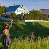 Person with a hat standing on a grassy hill with a house in the background