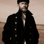 Man wearing a dark coat and hat in a sepia-toned landscape
