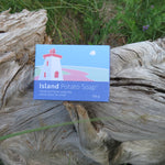 Box of Island Potato Soap on a piece of driftwood with grass in the background