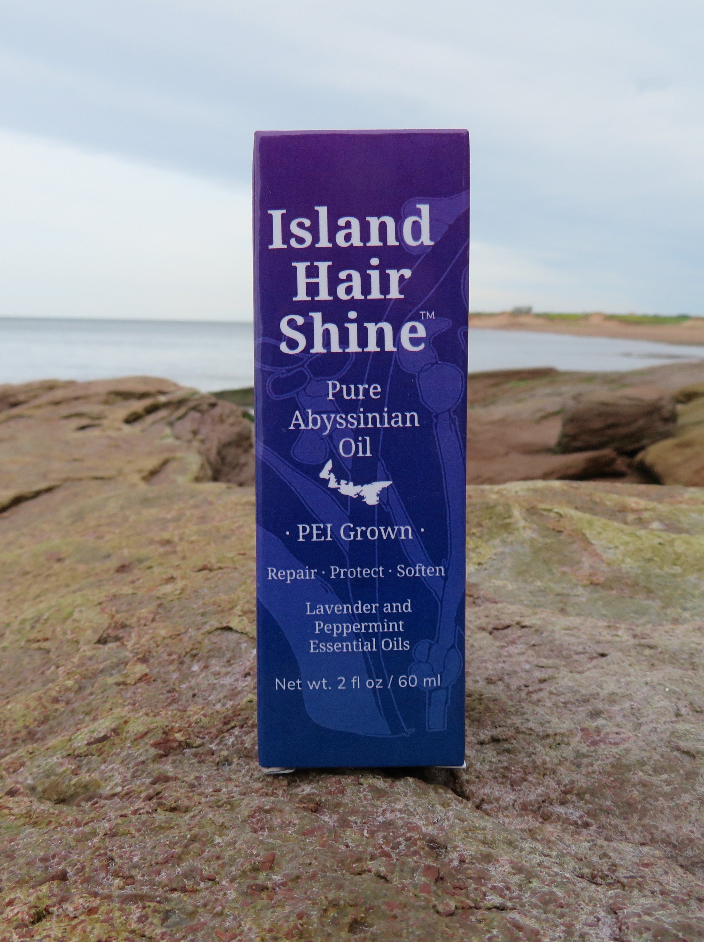 Island Hair Shine Pure Abyssinian Oil bottle on a rocky surface with a scenic background