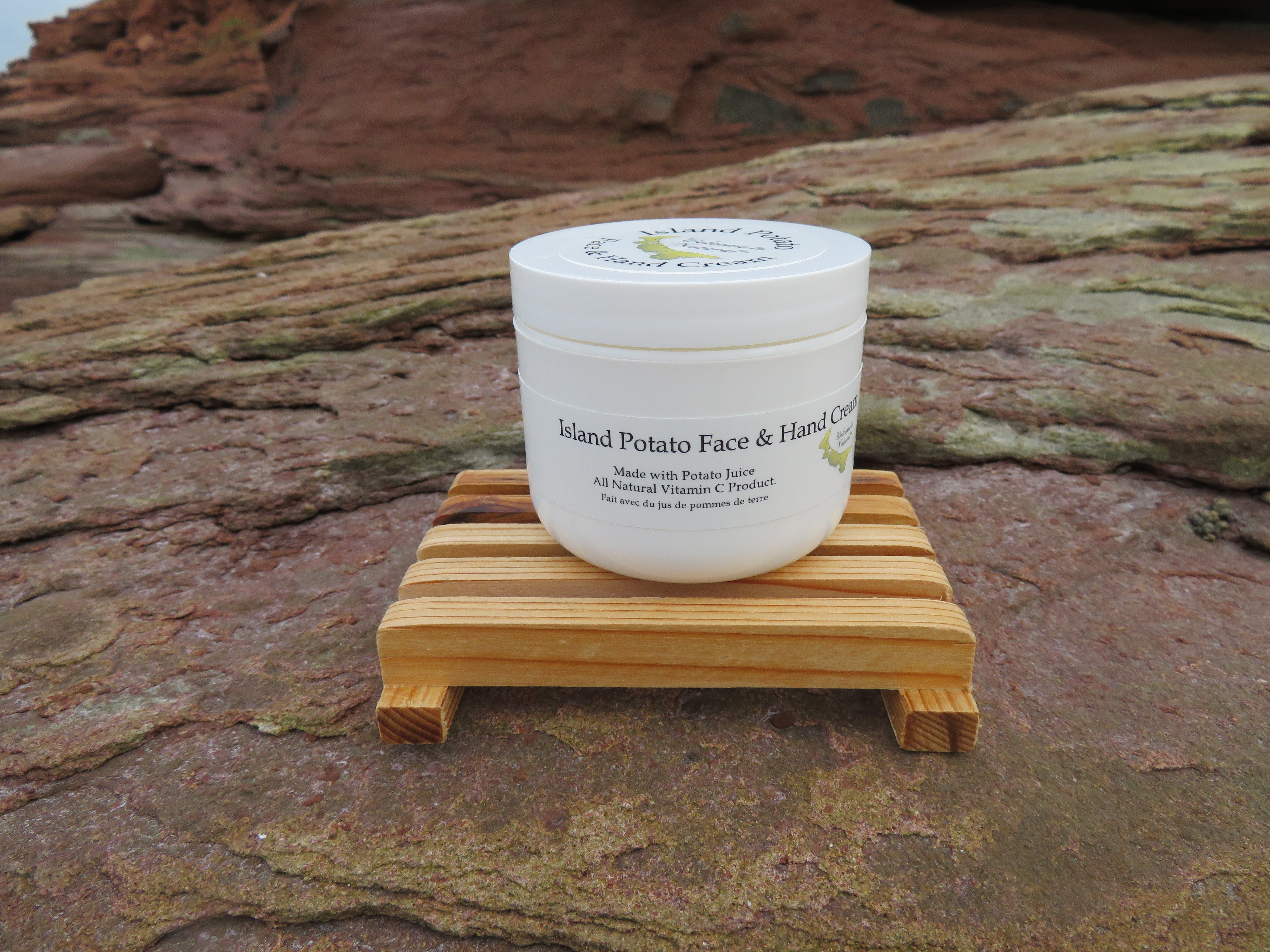 White jar of Island Potato Face & Hand Creme on a wooden stand with a natural rock background